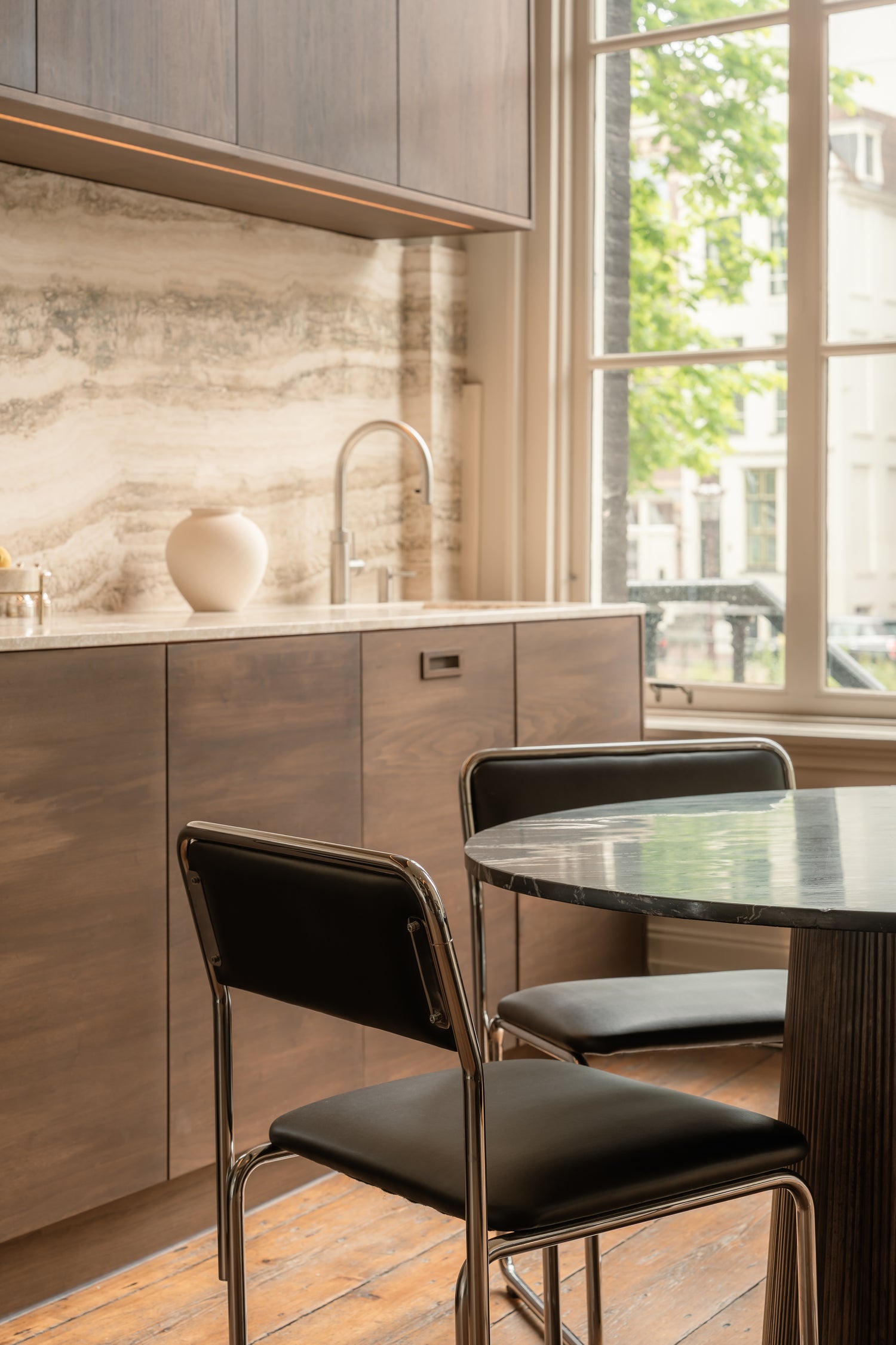 Modern kitchen with wooden cabinets, marble backsplash, and a dining table with chairs.